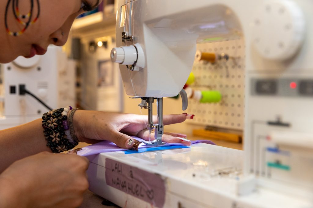 Close-up photo of a teenage girl concentrating as she leans over a sewing machine, hemming a piece of fabric.